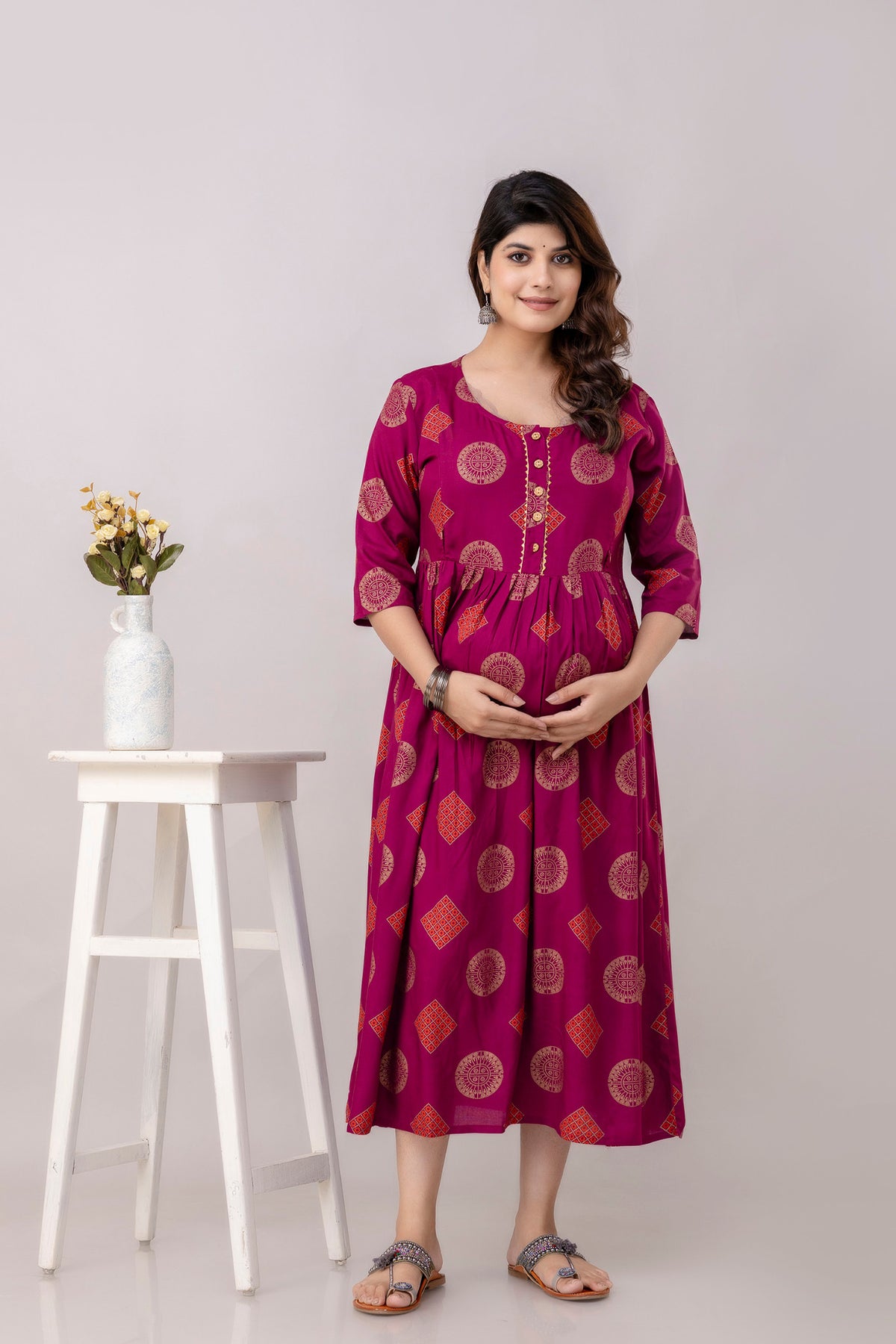 HENAL G-H417 wine printed maternity dress, full front view with hands below the bump, gold motifs and flared skirt.